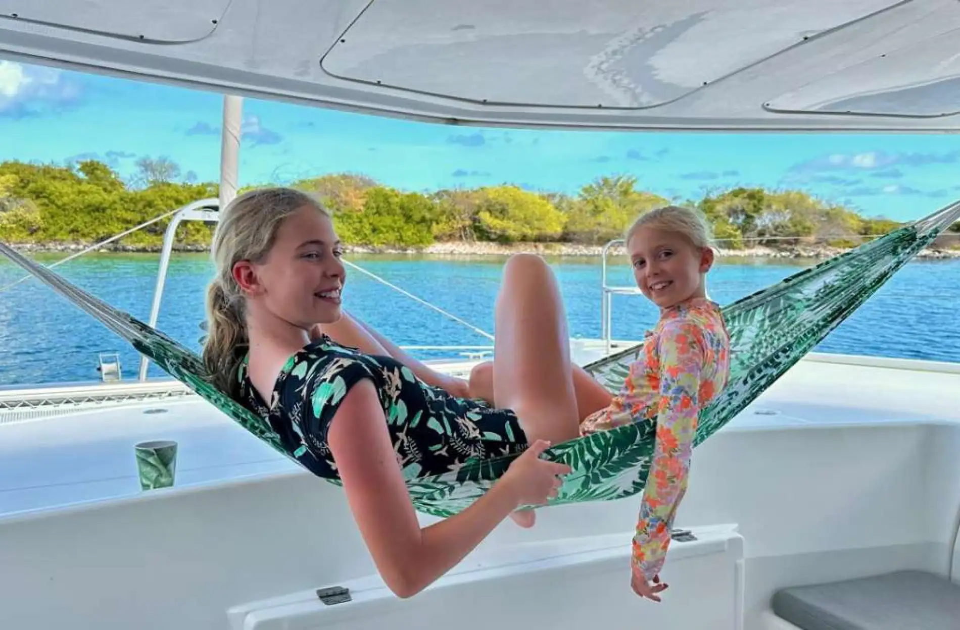 Girls in the hammock at anchor — Grenadines family charter Two girls relaxing in a hammock on a catamaran at anchor by a green Grenadine cay