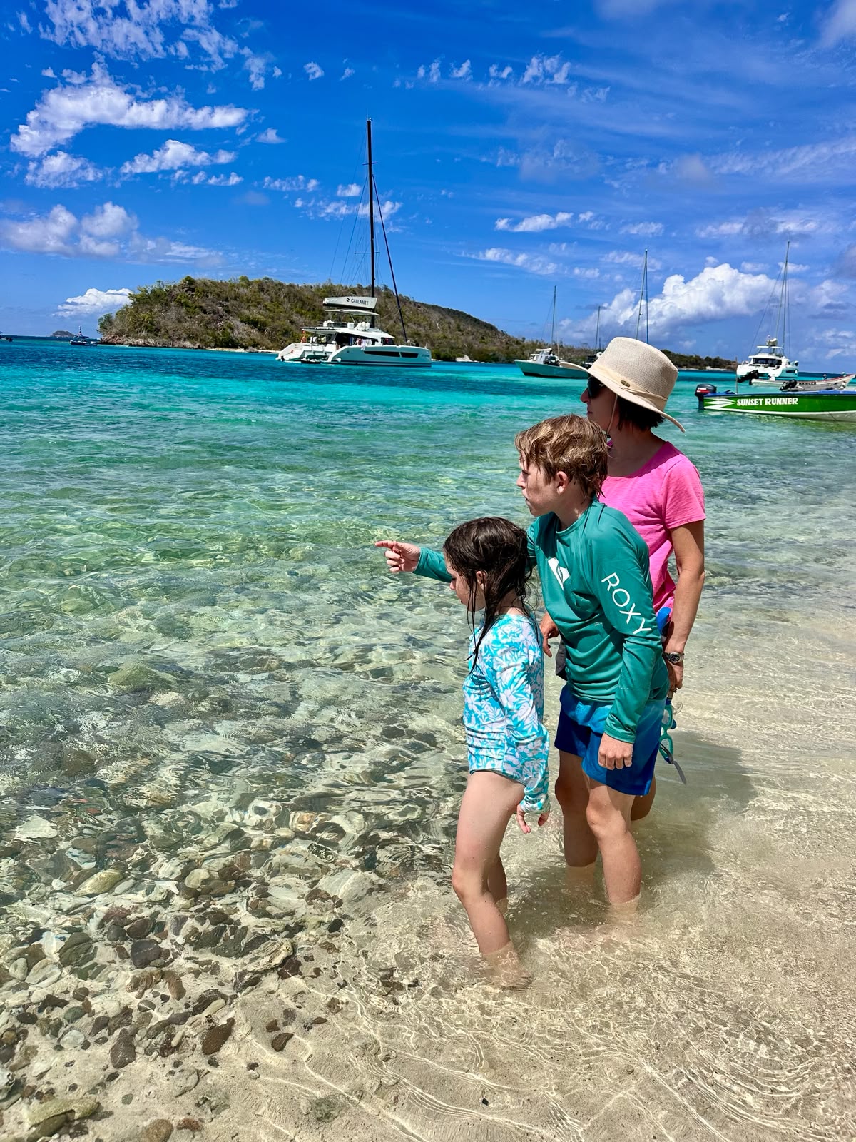 Mother and children wading in the turquoise shallows of the Tobago Cays with a catamaran at anchor