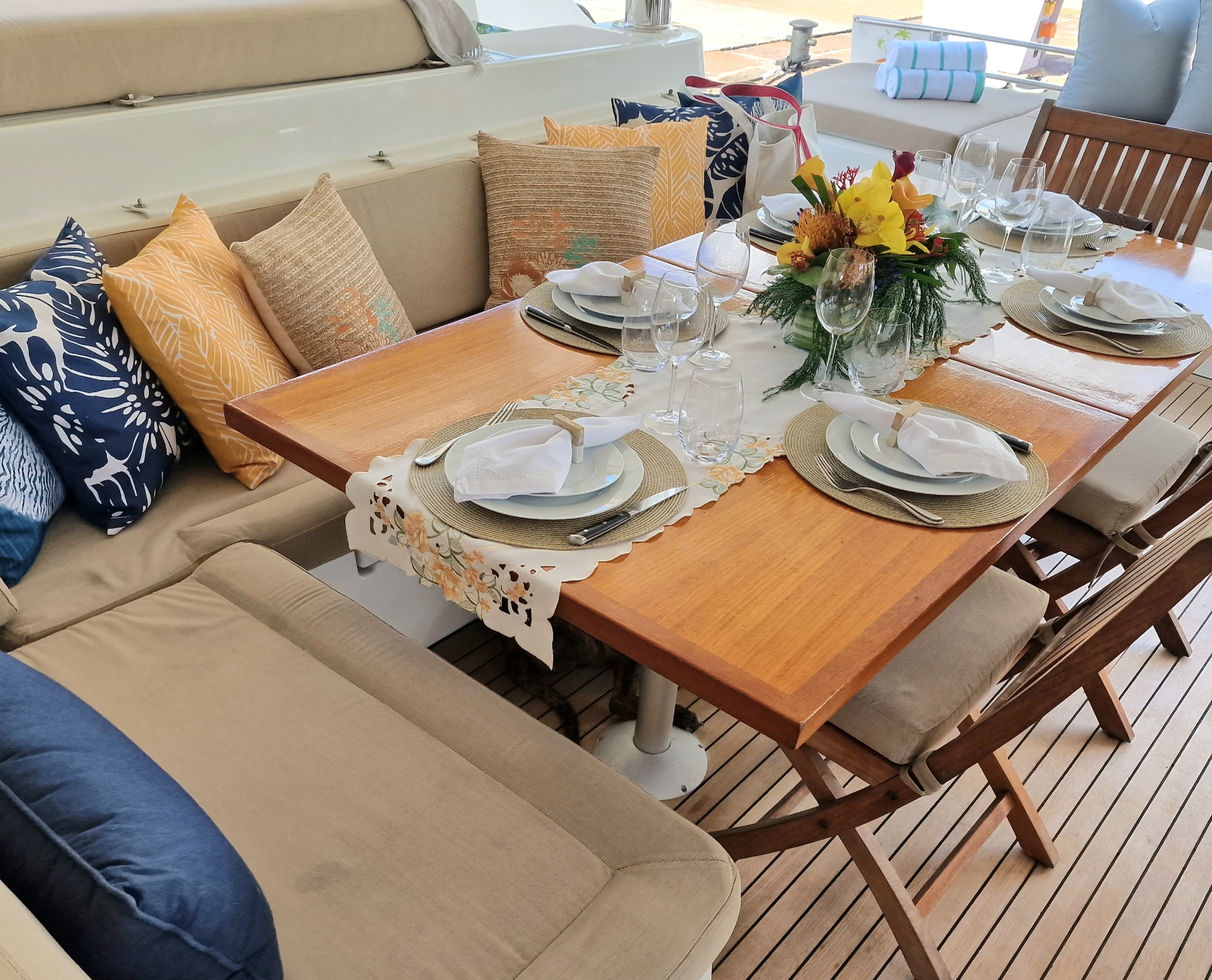 Lunch on the aft deck — crewed yacht charter, Grenadines Long teak dining table dressed for lunch on the aft deck of a crewed charter yacht at anchor in the Grenadines, with white linen, wine glasses and a tropical hillside backdrop