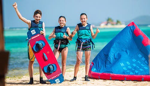 Three children on the beach in Union Island holding a kite before a kitesurfing session in the Grenadines