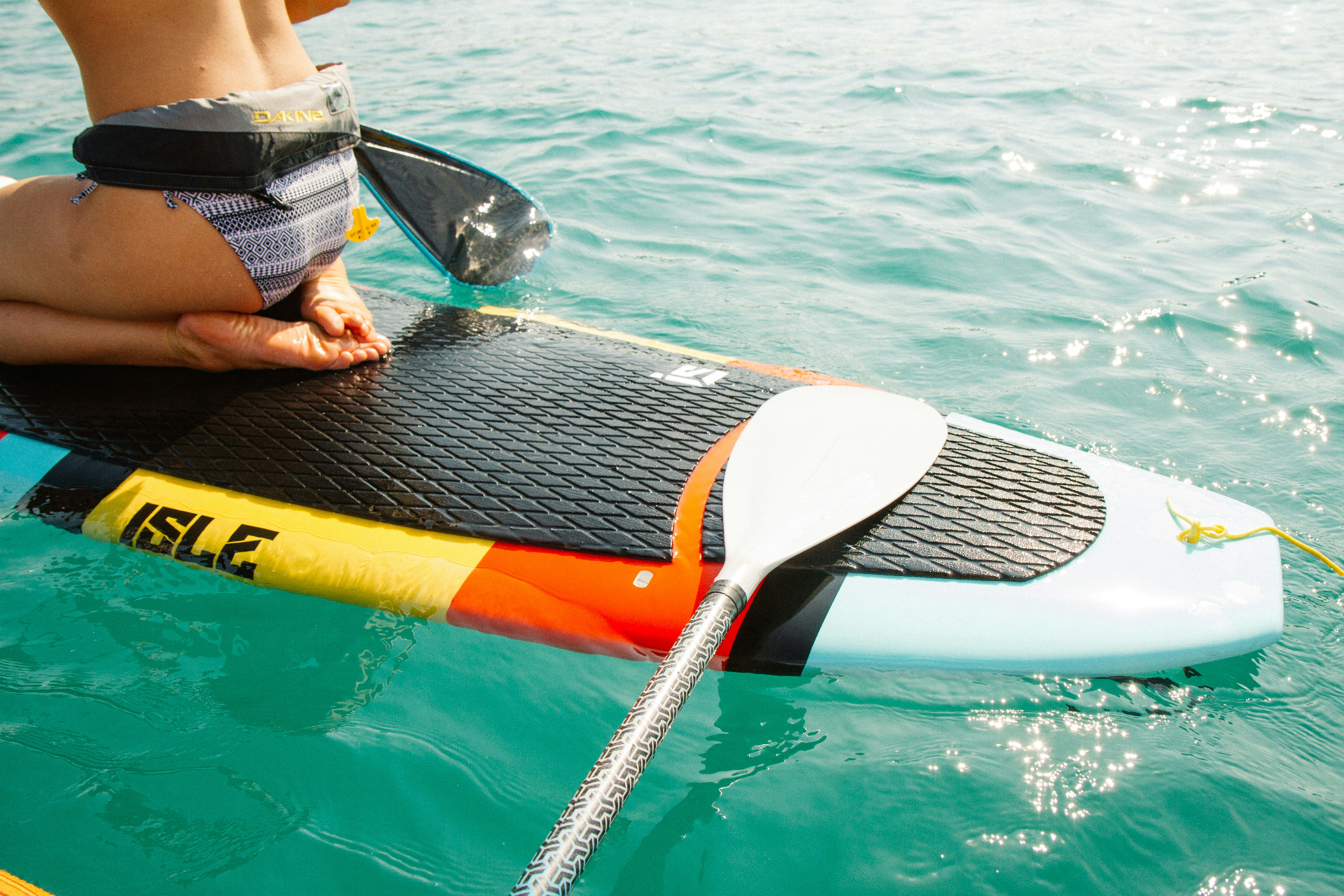 Paddleboarding around the anchorage on a Grenadines family charter Young paddleboarder sitting on a SUP in clear turquoise Caribbean water